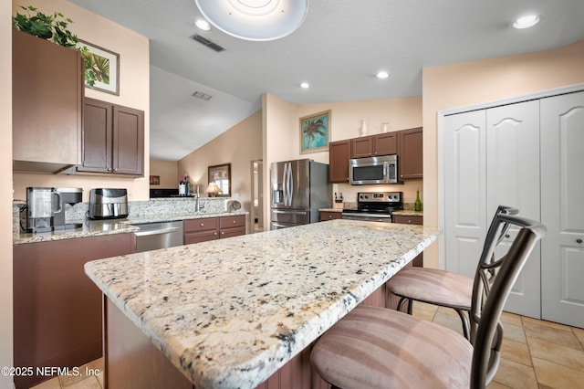 kitchen featuring appliances with stainless steel finishes, a kitchen island, a breakfast bar area, and lofted ceiling