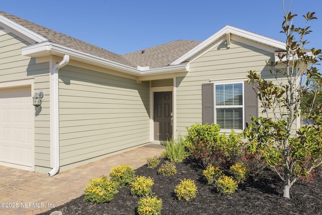 property entrance with an attached garage and roof with shingles