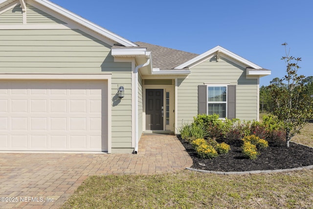 single story home featuring a garage, decorative driveway, and roof with shingles