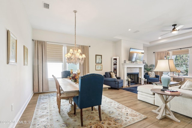 dining area featuring a fireplace, visible vents, wood finished floors, baseboards, and ceiling fan with notable chandelier