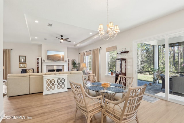 dining space featuring light wood finished floors, a fireplace, visible vents, and a tray ceiling