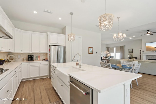 kitchen with a kitchen island with sink, white cabinetry, open floor plan, light countertops, and appliances with stainless steel finishes