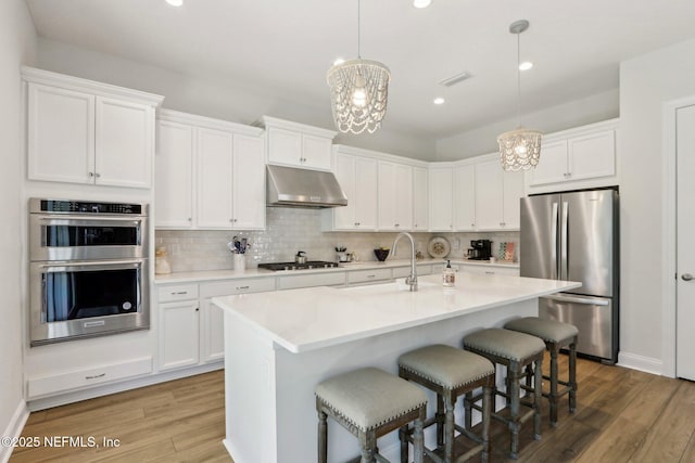 kitchen with under cabinet range hood, stainless steel appliances, white cabinets, light countertops, and decorative light fixtures