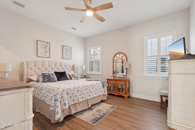 bedroom with a ceiling fan, visible vents, baseboards, and wood finished floors