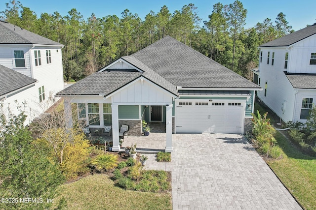 view of front facade with decorative driveway, a shingled roof, covered porch, board and batten siding, and a garage