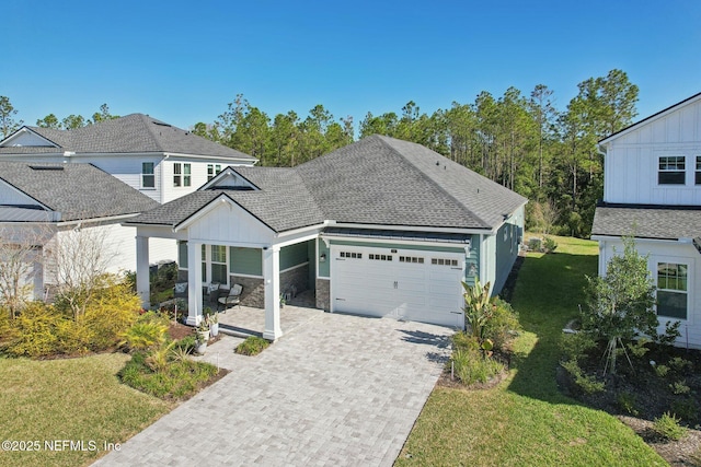 view of front of home with an attached garage, stone siding, decorative driveway, roof with shingles, and a front yard