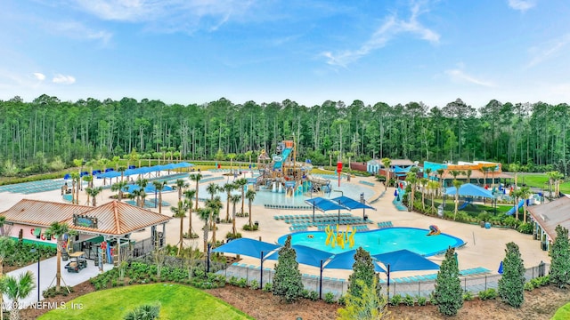 community pool with a water play area, fence, and a forest view