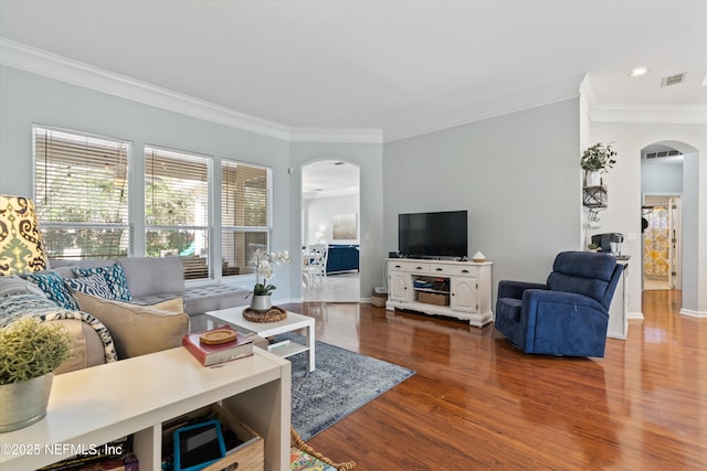 living room with arched walkways, wood finished floors, visible vents, baseboards, and crown molding