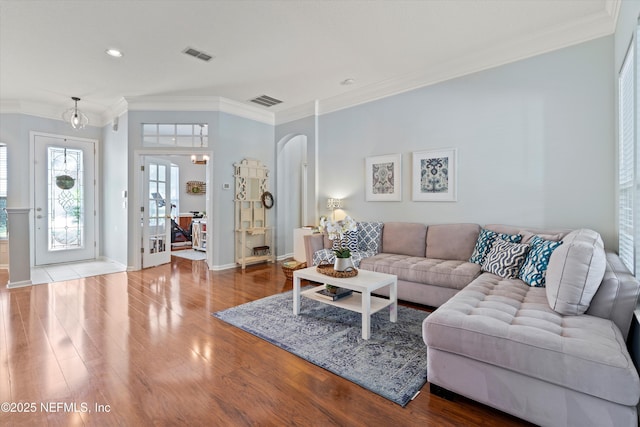 living area with ornamental molding, arched walkways, visible vents, and wood finished floors