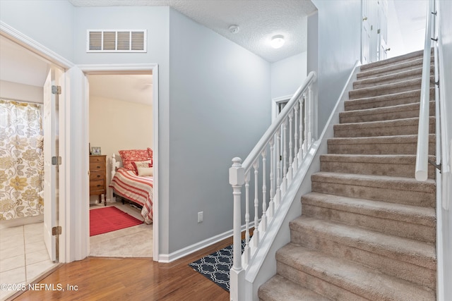 staircase featuring visible vents, a textured ceiling, baseboards, and wood finished floors