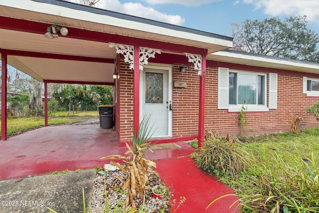 entrance to property featuring an attached carport, a patio area, brick siding, and driveway