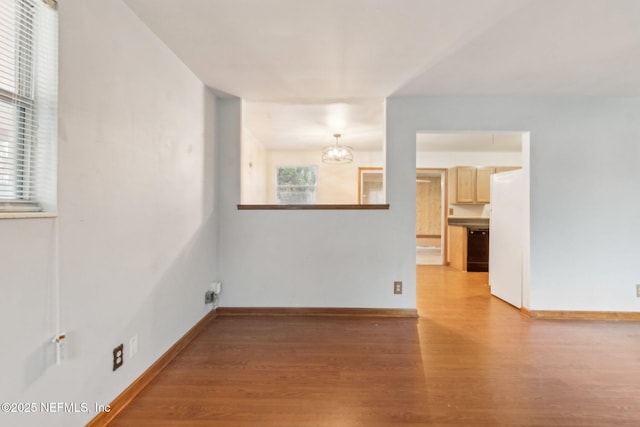 spare room featuring light wood-type flooring, a notable chandelier, and baseboards