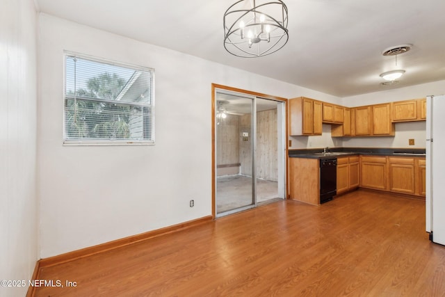 kitchen featuring black dishwasher, dark countertops, wood finished floors, decorative light fixtures, and a sink