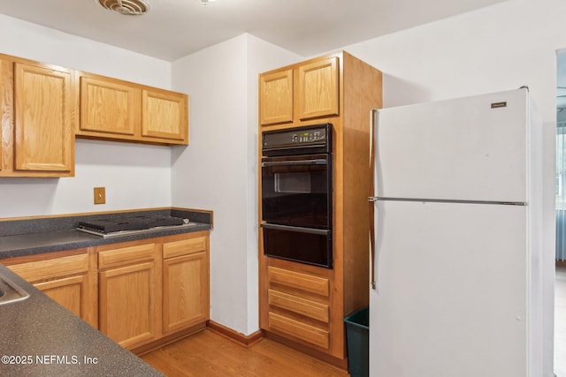 kitchen featuring freestanding refrigerator, a warming drawer, dark countertops, and light wood finished floors