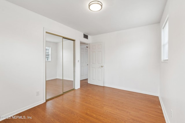 unfurnished bedroom featuring baseboards, a closet, visible vents, and wood finished floors