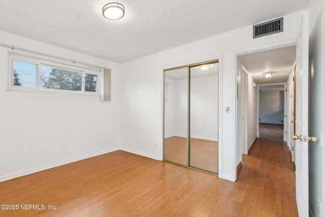 unfurnished bedroom featuring baseboards, a closet, visible vents, and wood finished floors