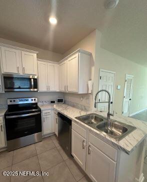 kitchen with stainless steel appliances, light countertops, white cabinets, a sink, and a peninsula