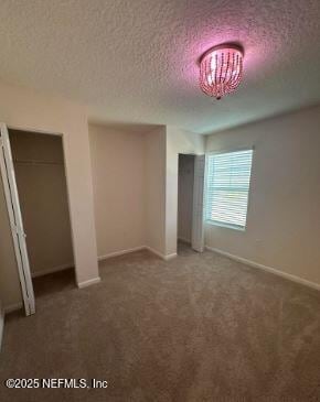 unfurnished bedroom featuring an inviting chandelier, carpet, baseboards, and a textured ceiling