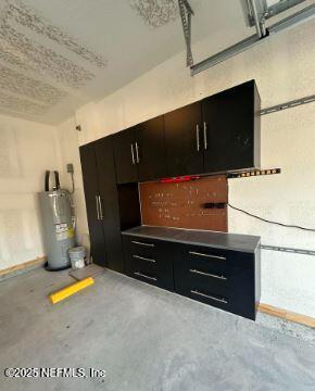 kitchen with water heater, dark cabinetry, and unfinished concrete floors