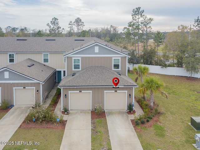 traditional-style home with a garage, fence, concrete driveway, roof with shingles, and a front yard