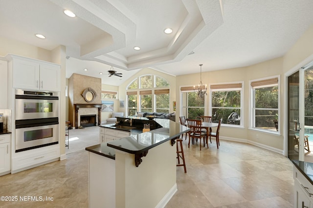 kitchen with open floor plan, double oven, a premium fireplace, and dark countertops