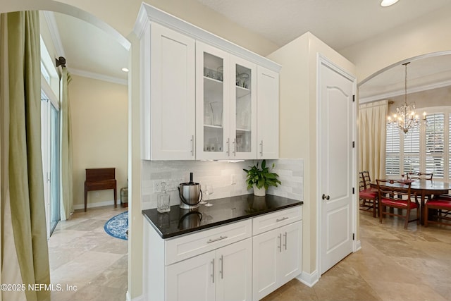 bar featuring arched walkways, a chandelier, hanging light fixtures, ornamental molding, and decorative backsplash