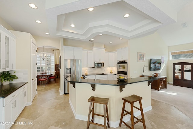 kitchen with arched walkways, stainless steel appliances, dark countertops, a raised ceiling, and a kitchen bar