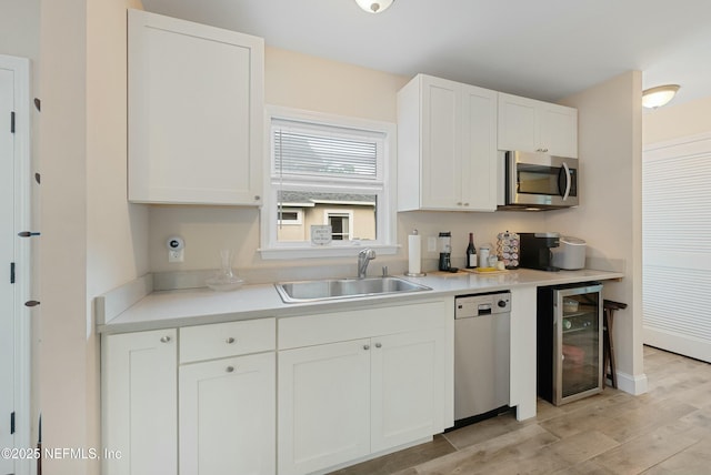 kitchen featuring stainless steel appliances, light wood-style flooring, white cabinetry, a sink, and beverage cooler