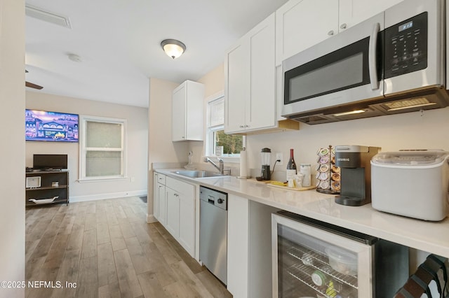 kitchen with stainless steel appliances, beverage cooler, white cabinets, and a sink