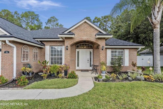 view of front of house featuring roof with shingles, brick siding, and a front lawn