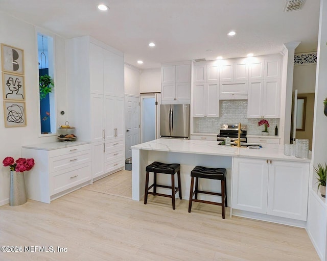 kitchen featuring visible vents, white cabinets, appliances with stainless steel finishes, a breakfast bar area, and a sink