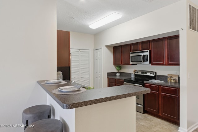 kitchen featuring dark brown cabinets, appliances with stainless steel finishes, dark countertops, and a peninsula