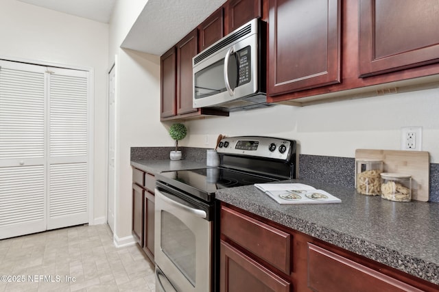 kitchen with appliances with stainless steel finishes, dark countertops, and reddish brown cabinets