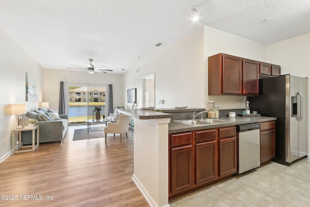 kitchen featuring dark countertops, appliances with stainless steel finishes, open floor plan, a sink, and a peninsula