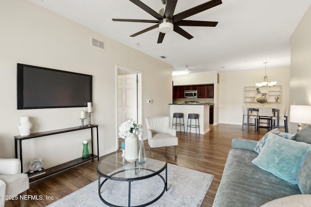 living area featuring ceiling fan with notable chandelier, dark wood-style flooring, visible vents, and baseboards