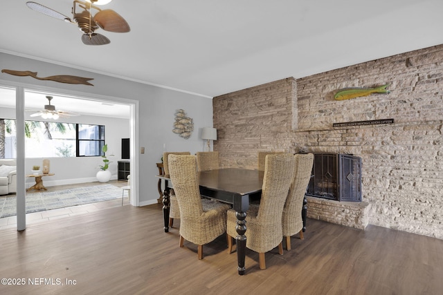 dining space featuring baseboards, a fireplace, ornamental molding, and wood finished floors