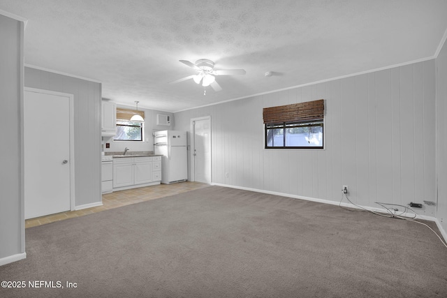 unfurnished living room featuring light carpet, ceiling fan, a textured ceiling, and crown molding