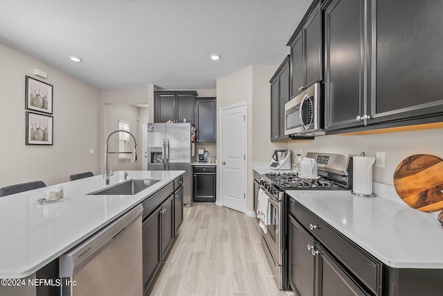 kitchen with sink, light wood-type flooring, appliances with stainless steel finishes, a textured ceiling, and a center island with sink