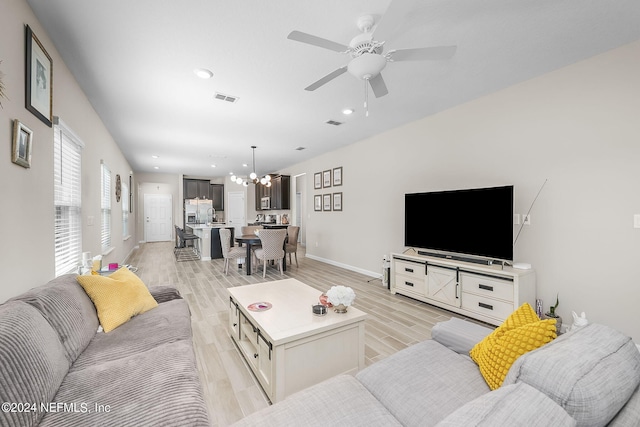 living room with light wood-type flooring and ceiling fan with notable chandelier