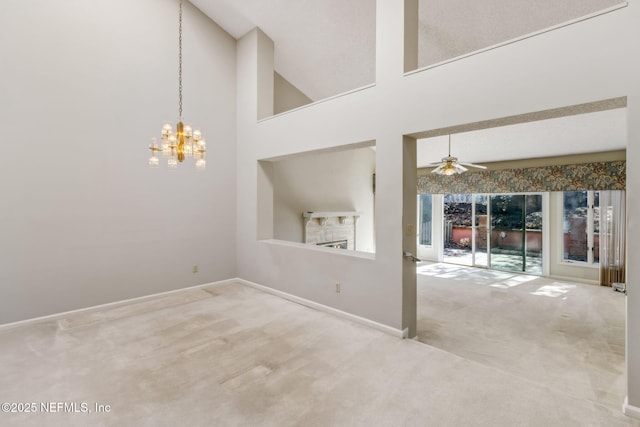 carpeted spare room featuring a towering ceiling, a lit fireplace, baseboards, and ceiling fan with notable chandelier