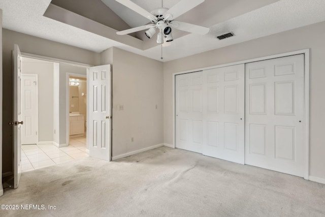 unfurnished bedroom with a tray ceiling, a closet, light colored carpet, visible vents, and baseboards