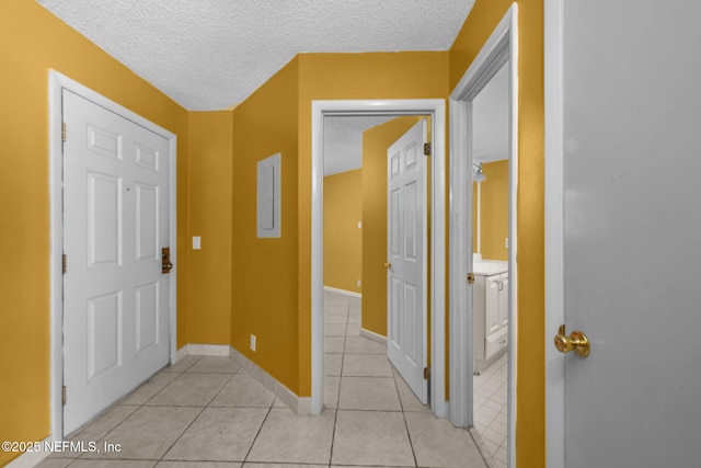 hallway with a textured ceiling, light tile patterned flooring, electric panel, and baseboards