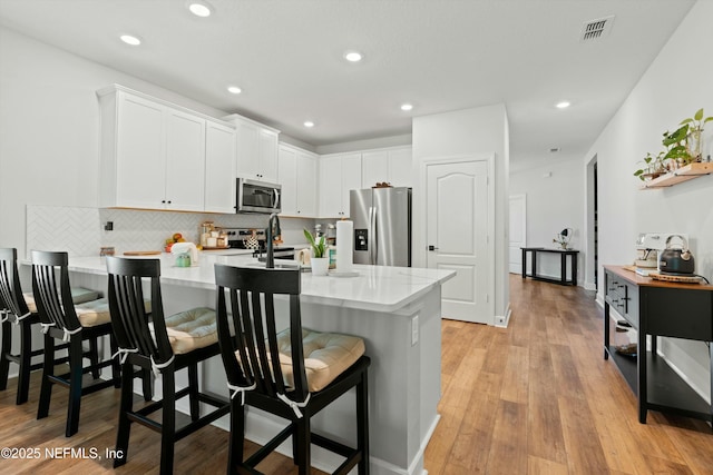 kitchen featuring stainless steel appliances, visible vents, light wood finished floors, and a kitchen bar