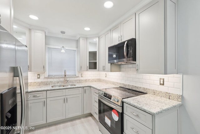 kitchen featuring light stone counters, stainless steel appliances, a sink, hanging light fixtures, and glass insert cabinets