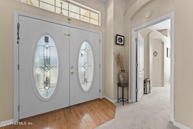 carpeted foyer entrance with arched walkways, baseboards, and wood finished floors