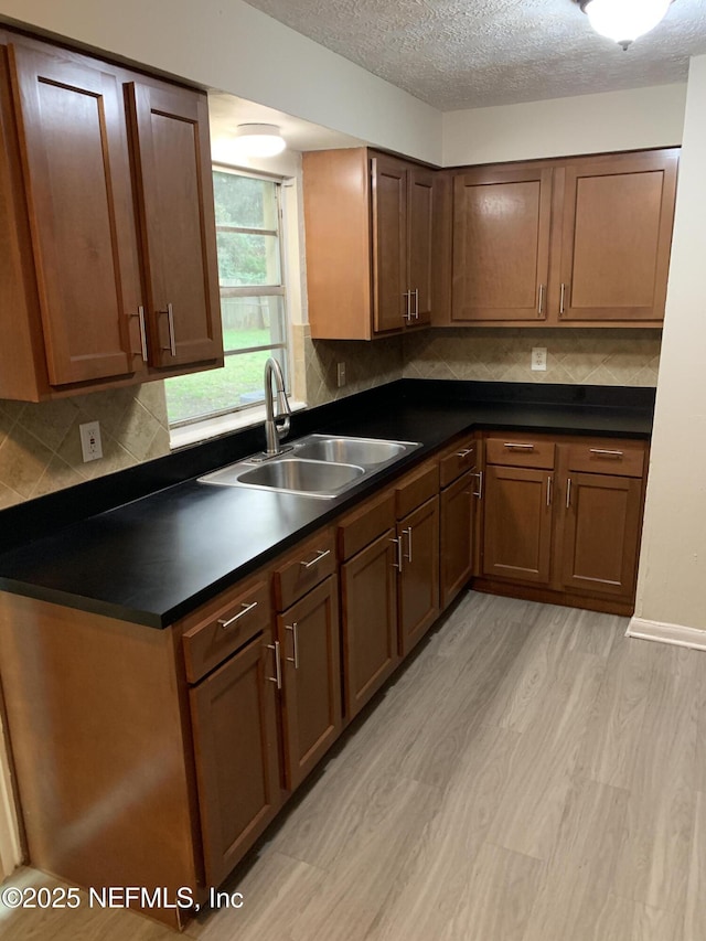 kitchen featuring light wood finished floors, dark countertops, backsplash, a sink, and a textured ceiling