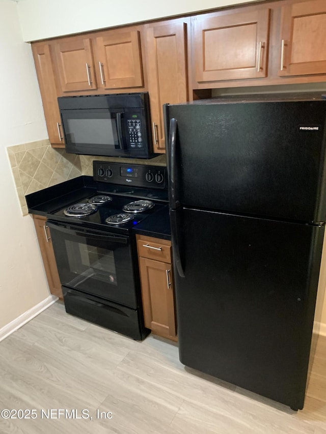 kitchen featuring dark countertops, black appliances, light wood-style flooring, and baseboards