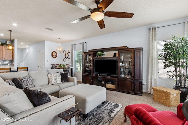 living room with light carpet, baseboards, visible vents, a ceiling fan, and a textured ceiling