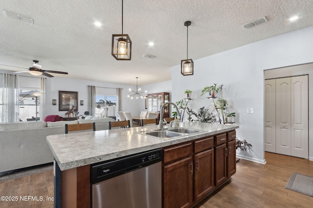 kitchen featuring a center island with sink, dishwasher, open floor plan, light countertops, and a sink