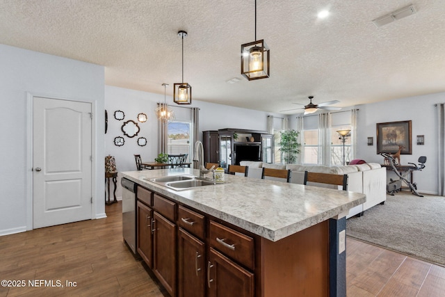 kitchen with open floor plan, a kitchen island with sink, light countertops, pendant lighting, and a sink